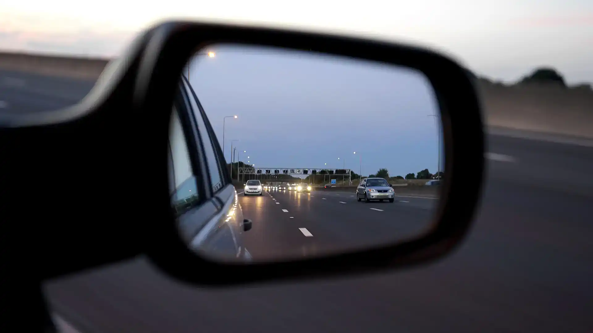 San Antonio police car mirror showing highway traffic at dusk.