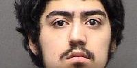 Mugshot of young man with dark curly hair and tattoos, wanted by San Antonio Crime Stoppers.