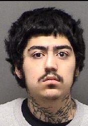 Mugshot of young man with dark curly hair and tattoos, wanted by San Antonio Crime Stoppers.