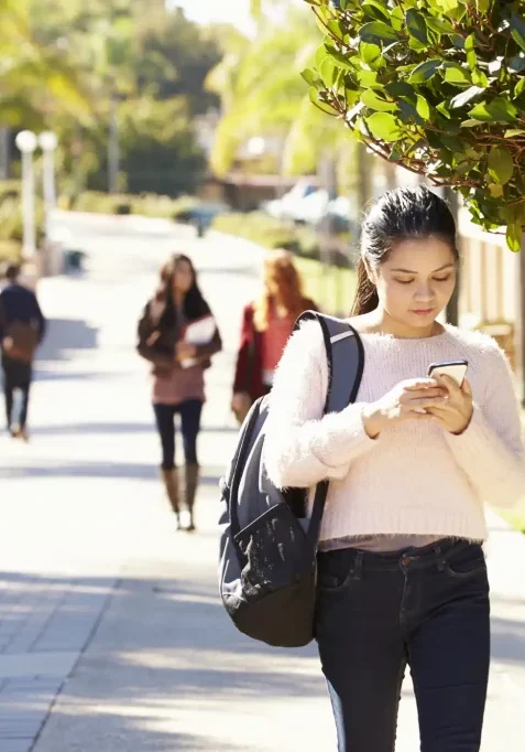 Young woman using her phone on a city sidewalk, promoting San Antonio Crime Stoppers.