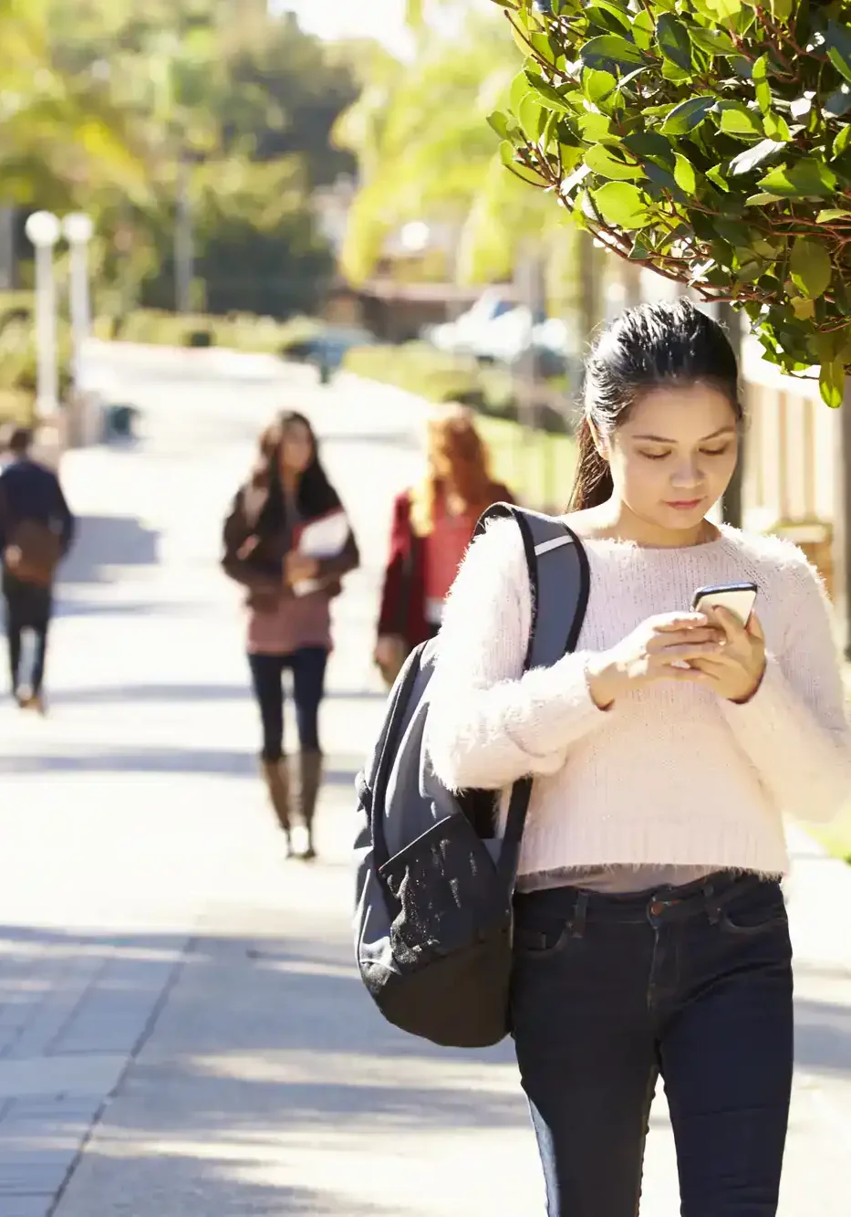 Young woman using her phone on a city sidewalk, promoting San Antonio Crime Stoppers.